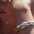 Bild på kvinna med handen över ansiktet. Solen lyser. Kvinnan har rosa nagel på tummen. Goddess örhänge i örat och bär två armband från OYS i guld och silver. 